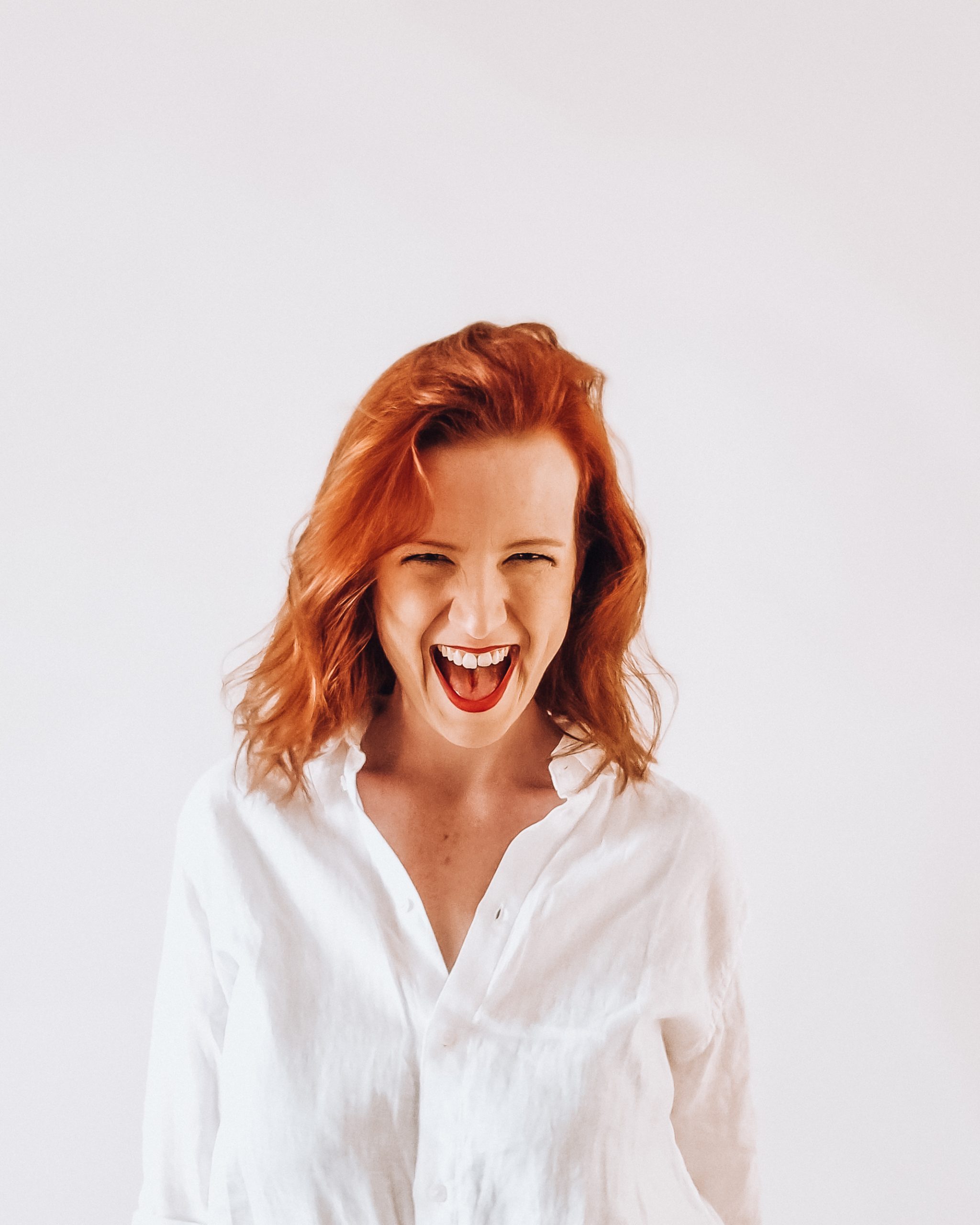 About me A redhead woman in a white shirt looking straight into camera smiling