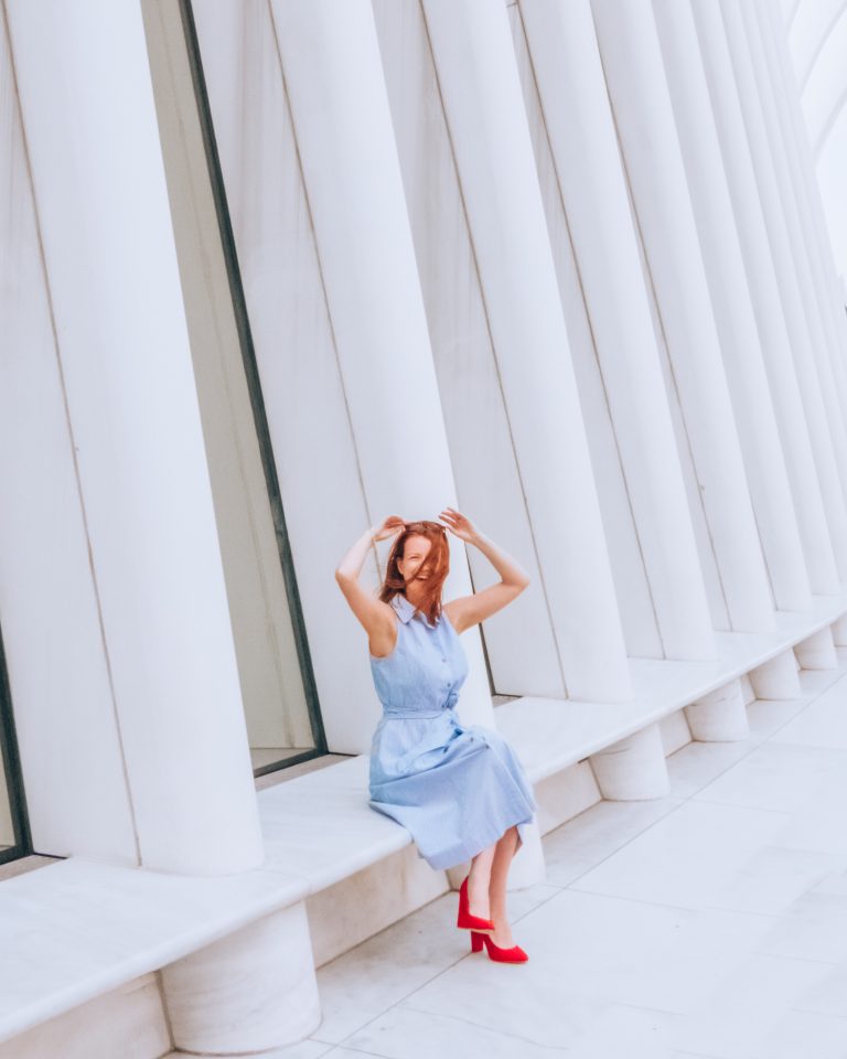 Woman in blue dress and red heels in sitting in front of Oculus New York