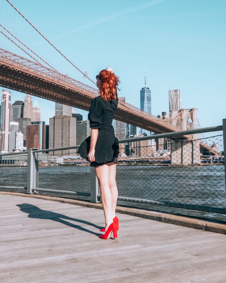 About me A redhead in a black dress and red heels overlooking the Manhattan skyline and Brooklyn bridge. Brooklyn Bridge guide