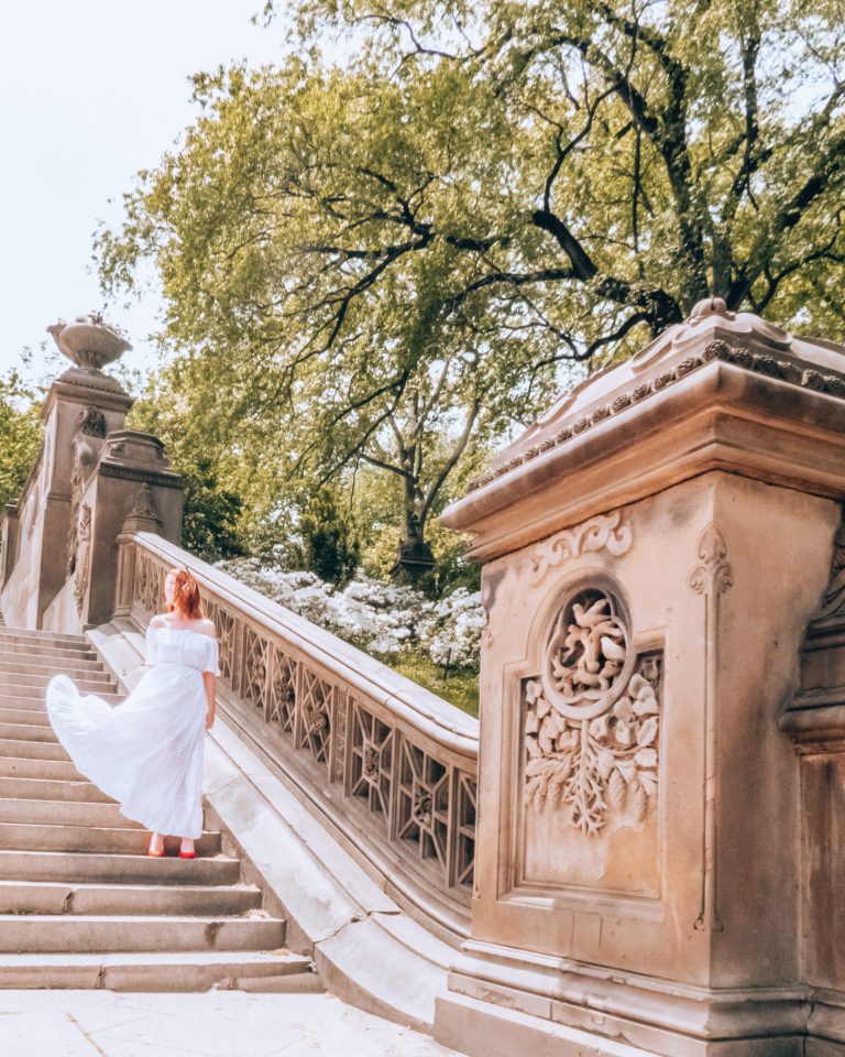 A woman in a long white dress and red heels standing on old city stairs