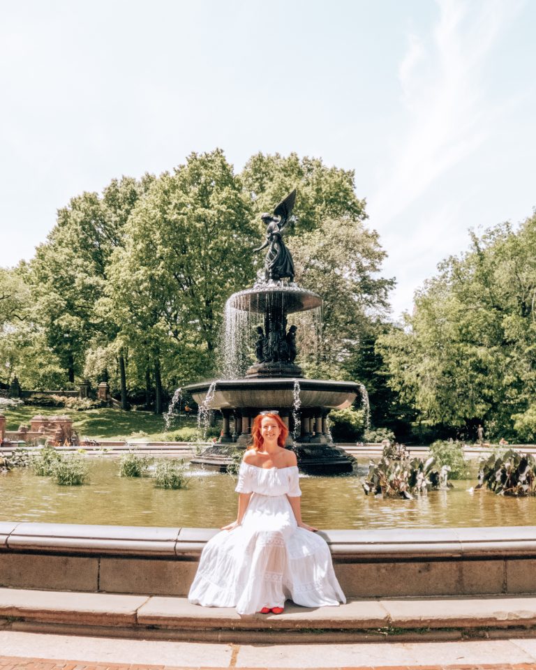 About me A woman in a long white dress and red heels sitting on side of Bethesda fountain in Central Park