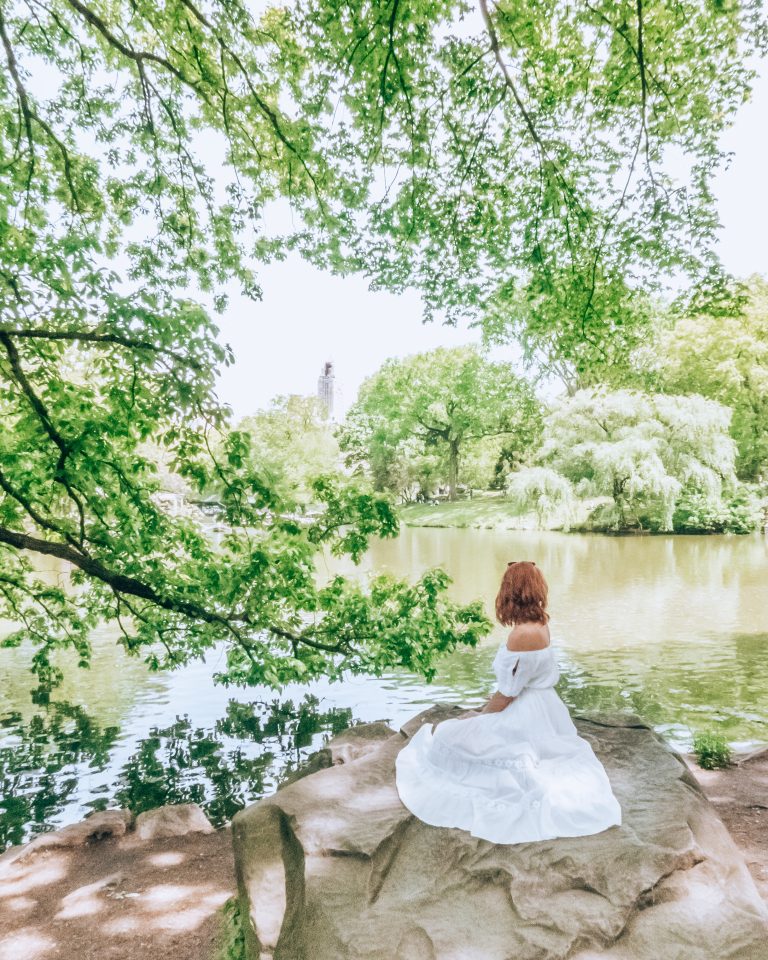 Woman in a long white dress sitting on a rock by water in Central Park