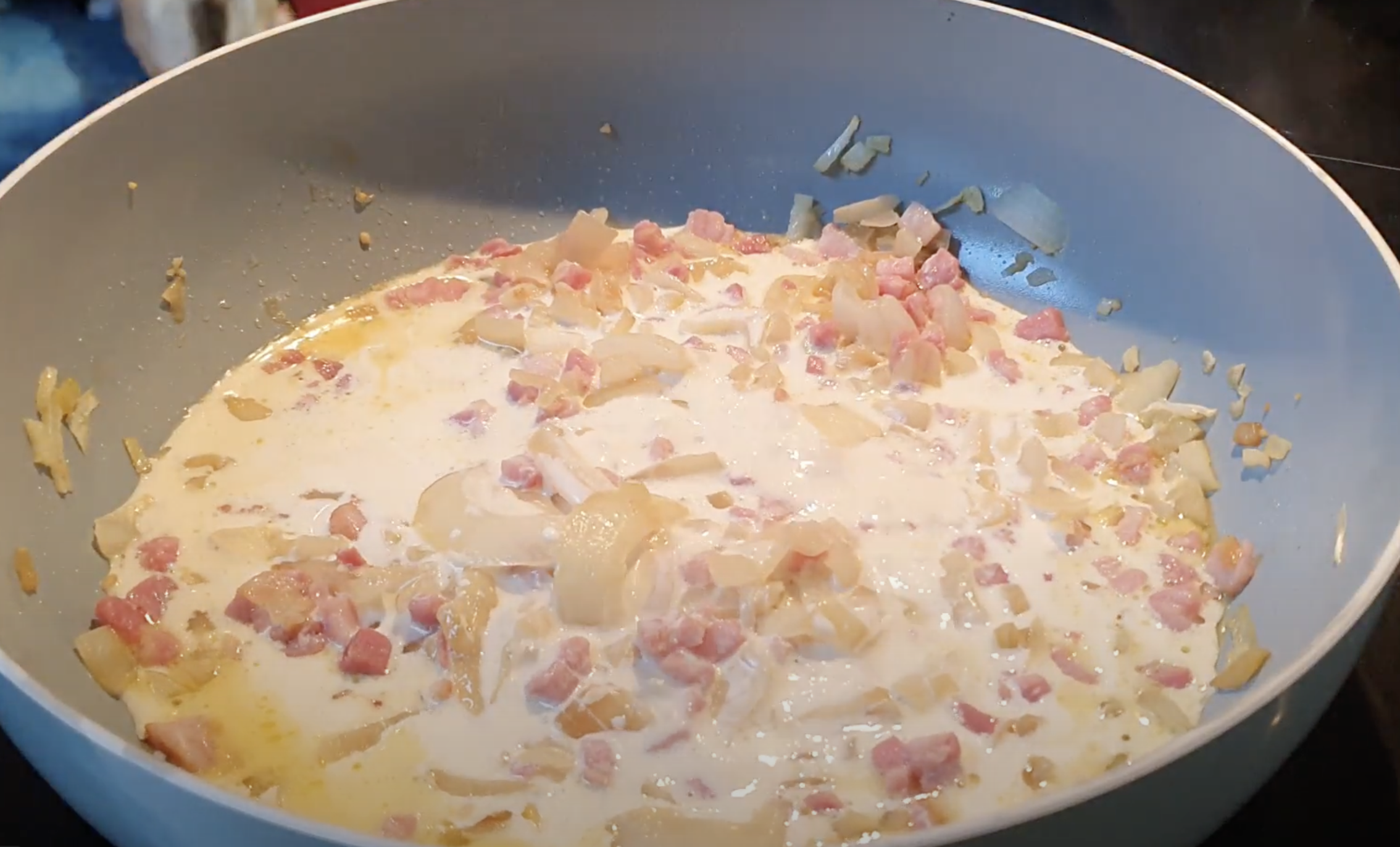 Blue frying pan with bacon, onion and cream cooking